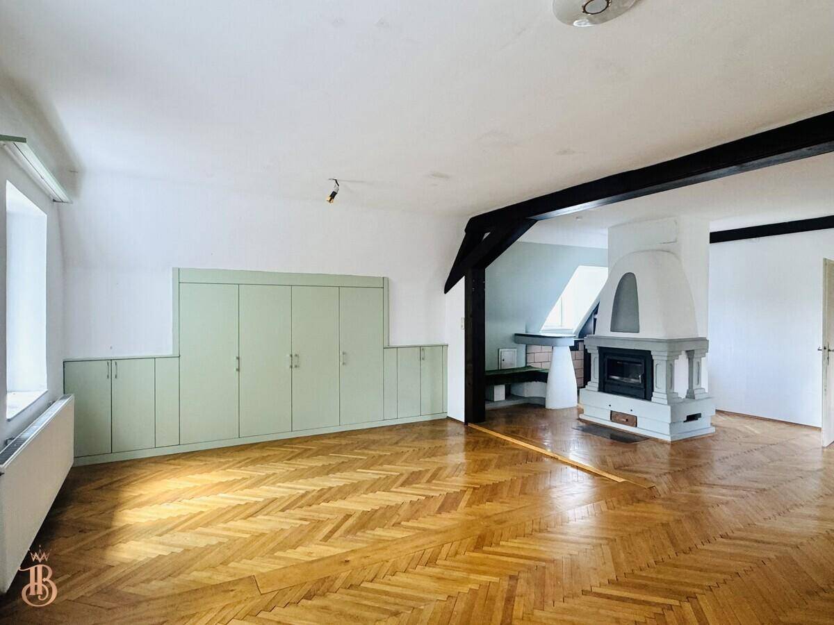 Helles Dachzimmer mit Kamin, Holzbalken und Einbauschränken, ideal als Wohn- oder Schlafbereich.