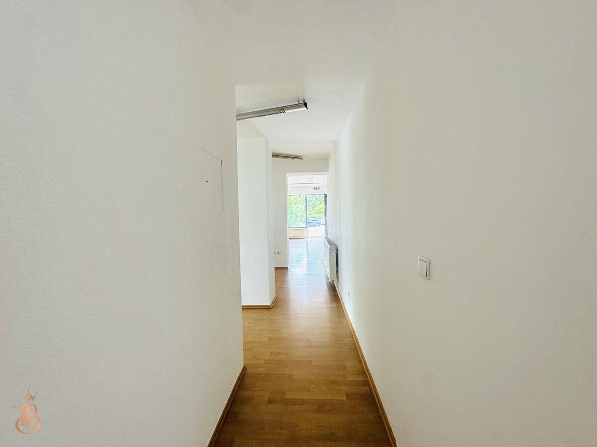 Langer, heller Flur mit Laminatboden und weiß gestrichenen Wänden, führt zu weiteren Räumen.