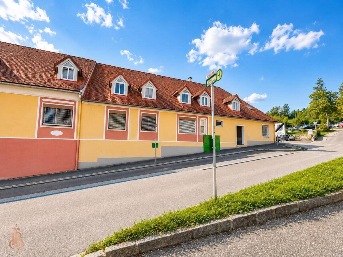 Gebäudeansicht entlang einer ansteigenden Straße mit grüner Umgebung.