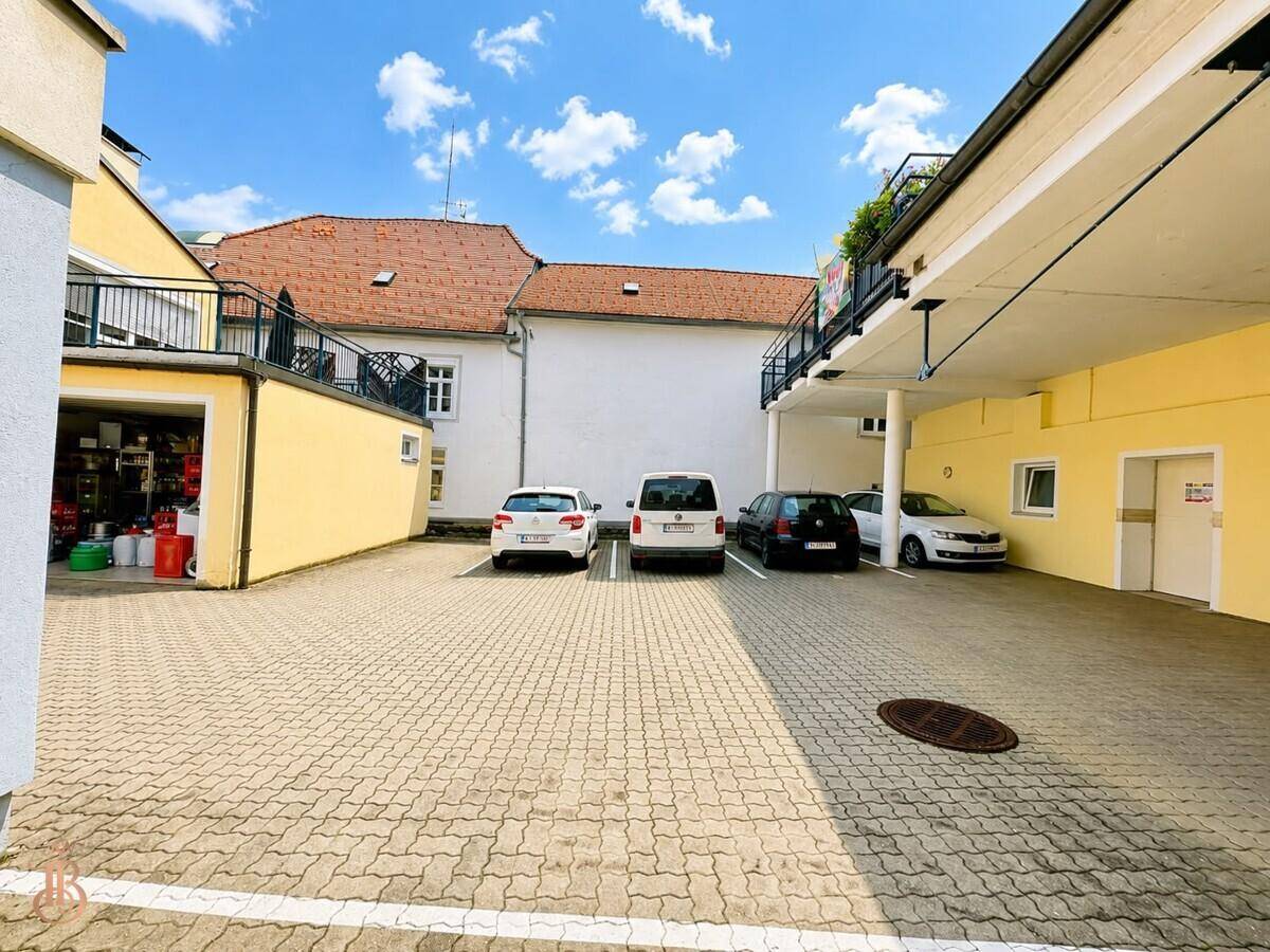 Außenparkplatz mit mehreren Autos und angrenzenden Gebäuden unter blauem Himmel.