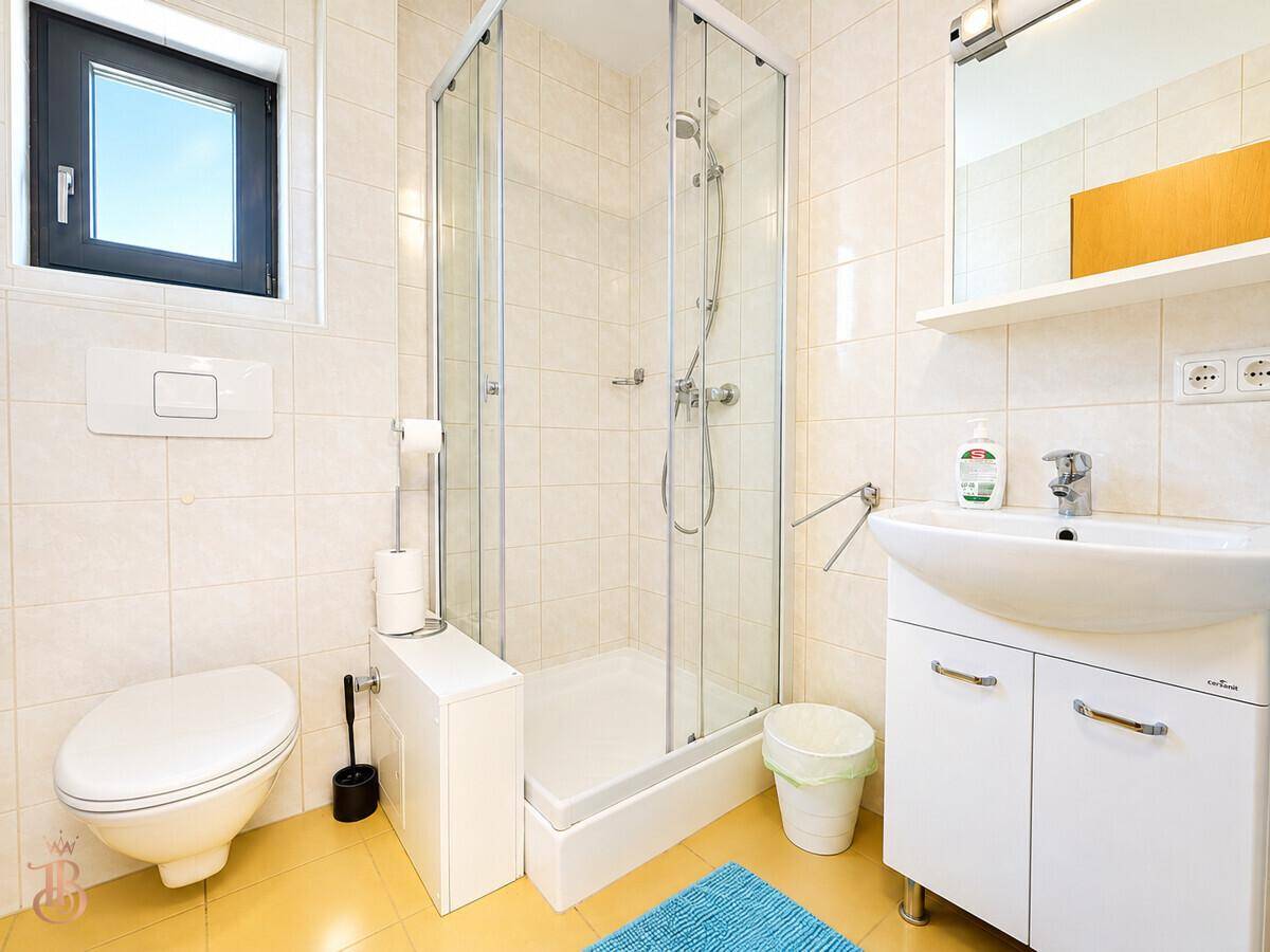 Helles Badezimmer mit Duschkabine, Toilette, Waschbecken und Fenster für frische Luft.