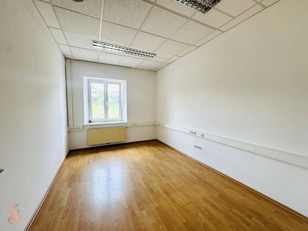 Kleinerer Büroraum mit Fenster, Laminatboden und weiß gestrichenen Wänden, hell und funktional.