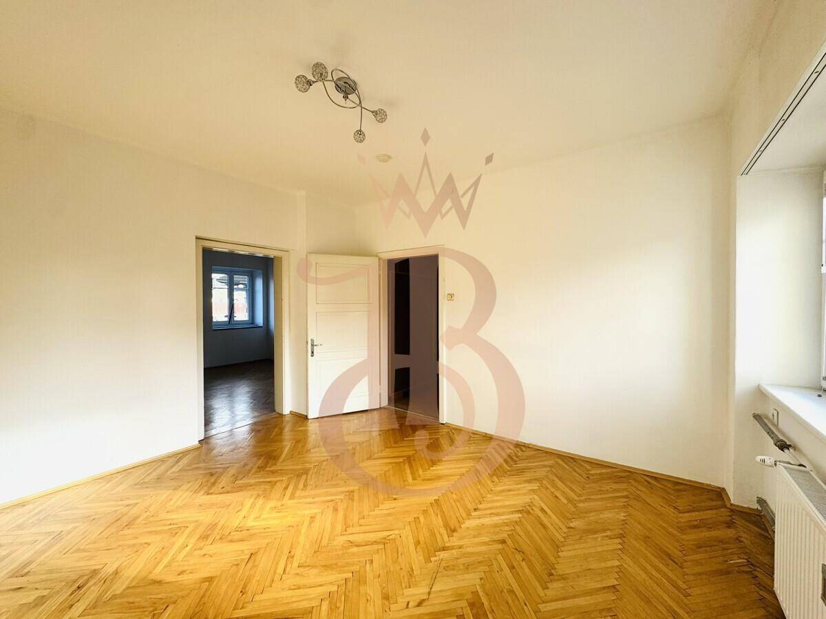 Helles Zimmer mit Fischgrätparkettboden und Zugang zu weiteren Räumen, gut beleuchtet.