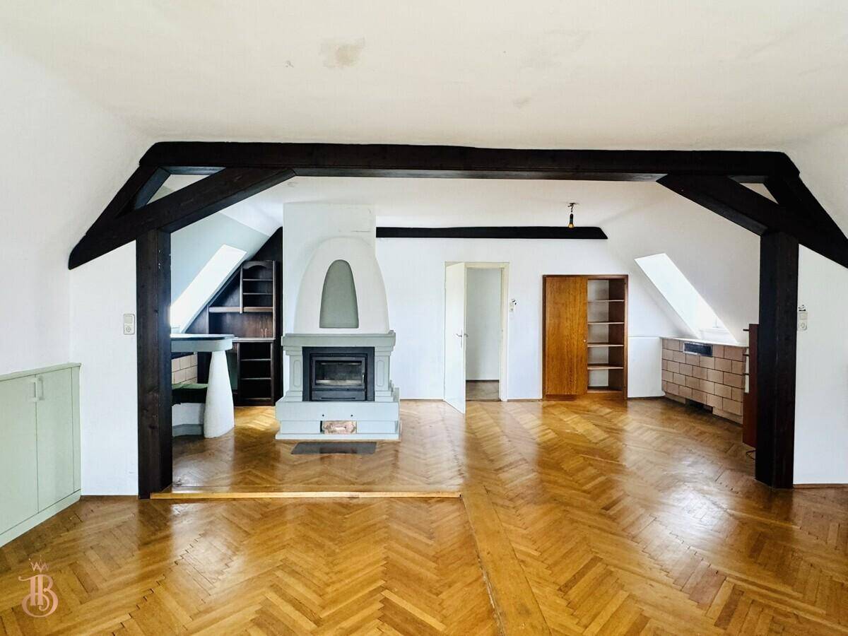 Dachzimmer mit Holzbalken, Kamin und Fischgrätparkett, das eine gemütliche Atmosphäre schafft.