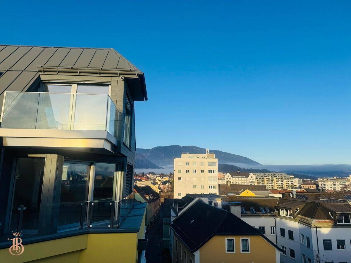 Moderne Gebäudefassade mit Glasbalkonen und weitem Blick über die Stadt und die umliegenden Berge.