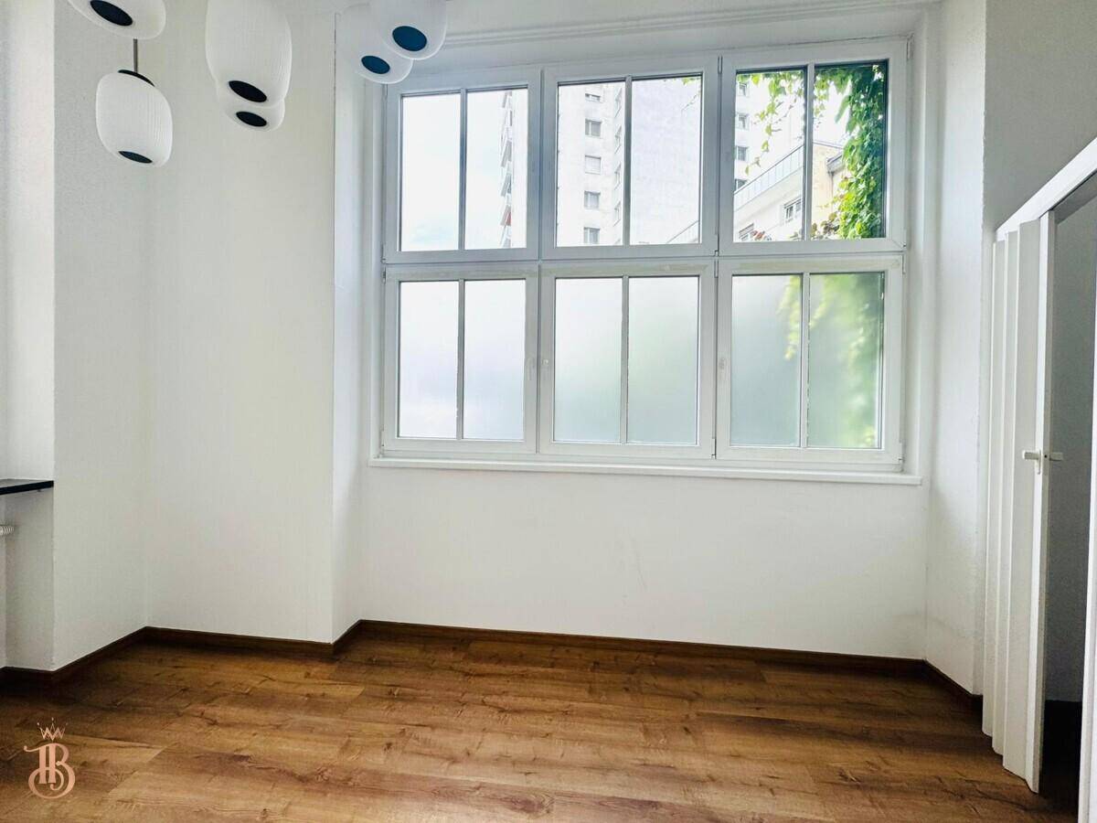 Helles Zimmer mit großem Fenster, Laminatboden und moderner Deckenleuchte.