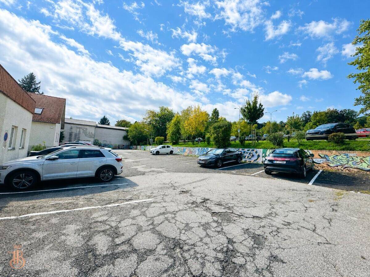 Großer Außenparkplatz mit mehreren Fahrzeugen und Bäumen im Hintergrund.