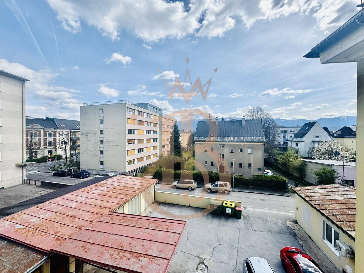 Blick auf die städtische Umgebung mit Gebäuden, Straßen und Bergen im Hintergrund unter blauem Himmel.
