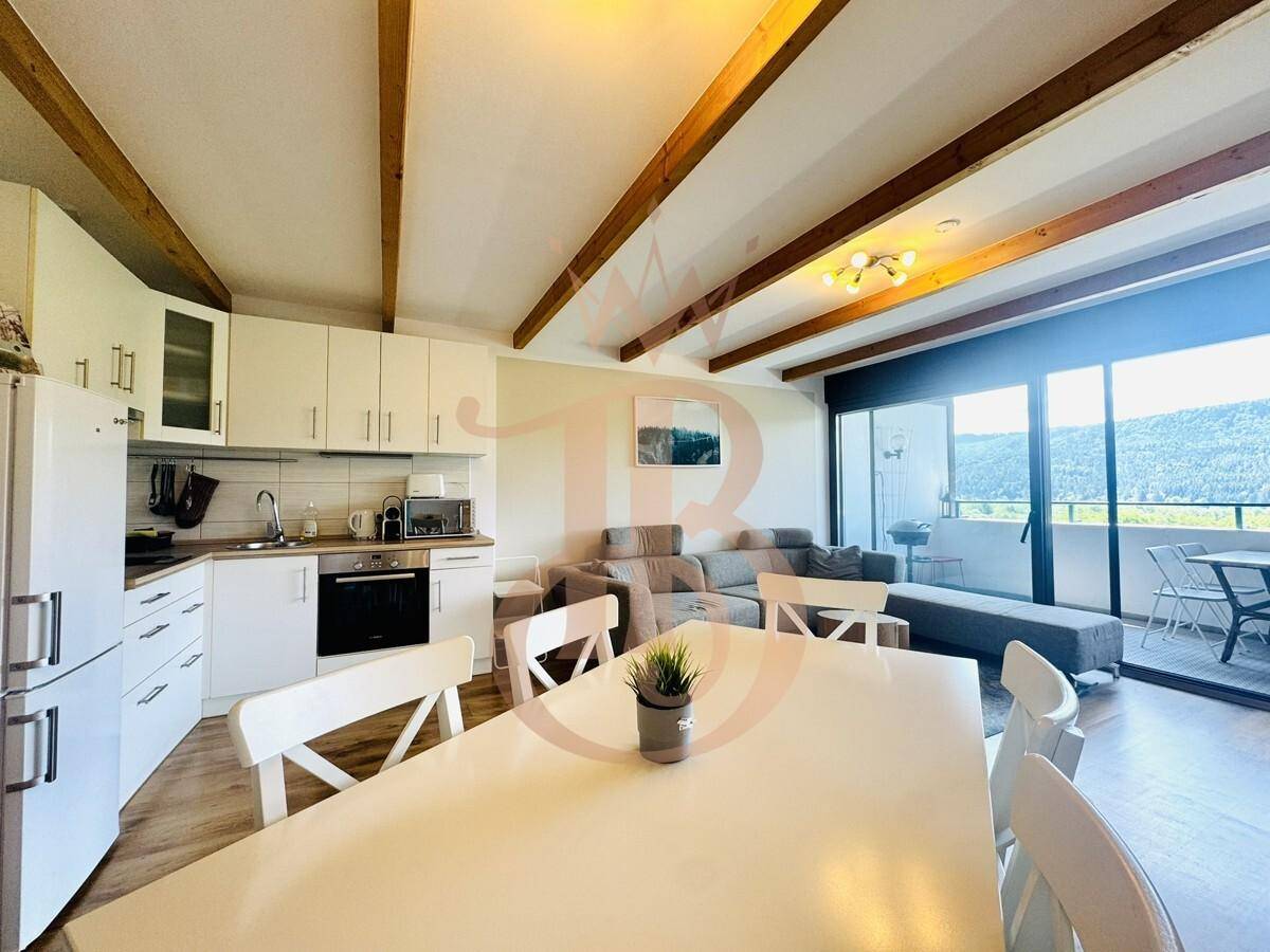 Offener Wohn-Essbereich mit integrierter Küche, Holzbalken und Zugang zum Balkon mit Aussicht.