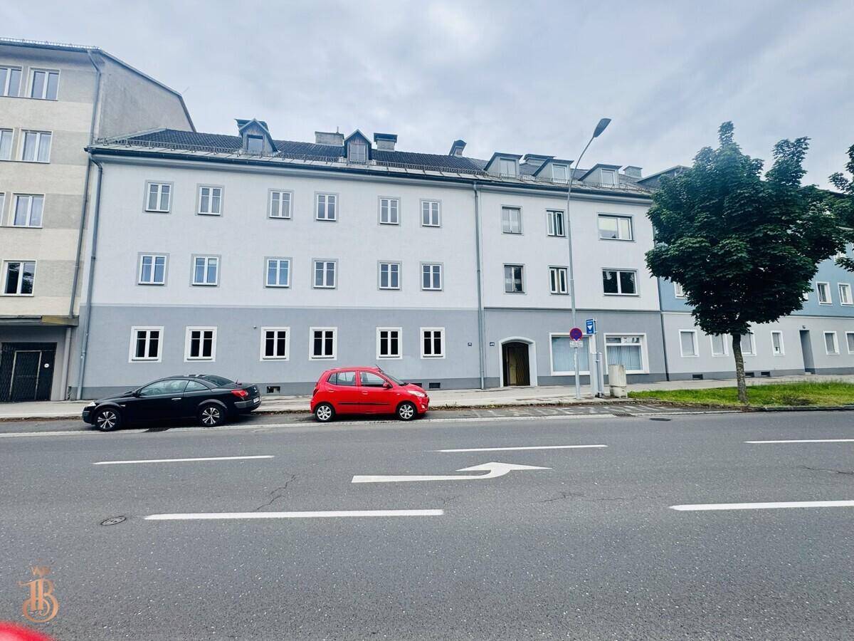 Ansicht der Gebäudefassade von der Straße mit parkenden Autos und bewölktem Himmel.