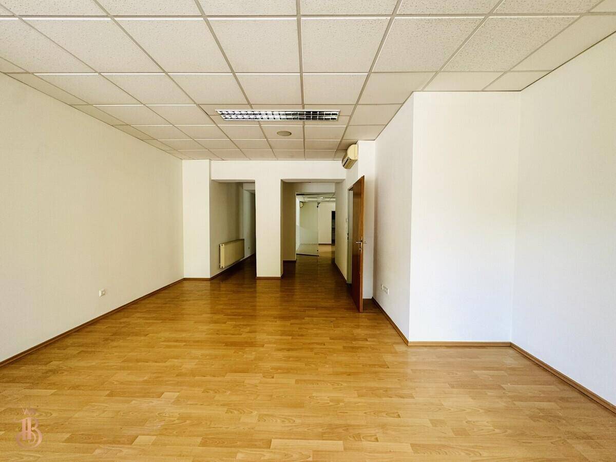 Heller Büroraum mit Holzfußboden, Klimaanlage und Blick in einen angrenzenden Flur.