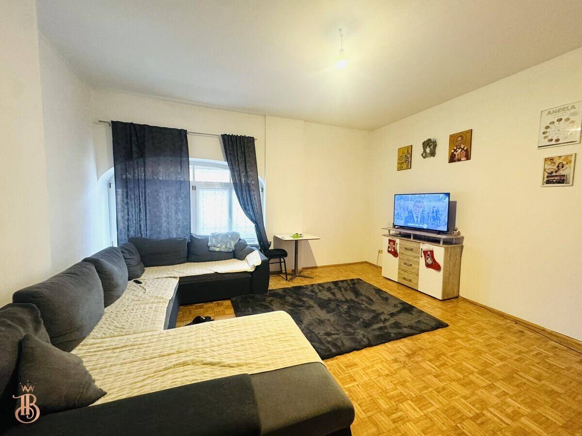 Gemütliches Wohnzimmer mit großem Ecksofa, Fernseher und Parkettboden, hell und einladend.