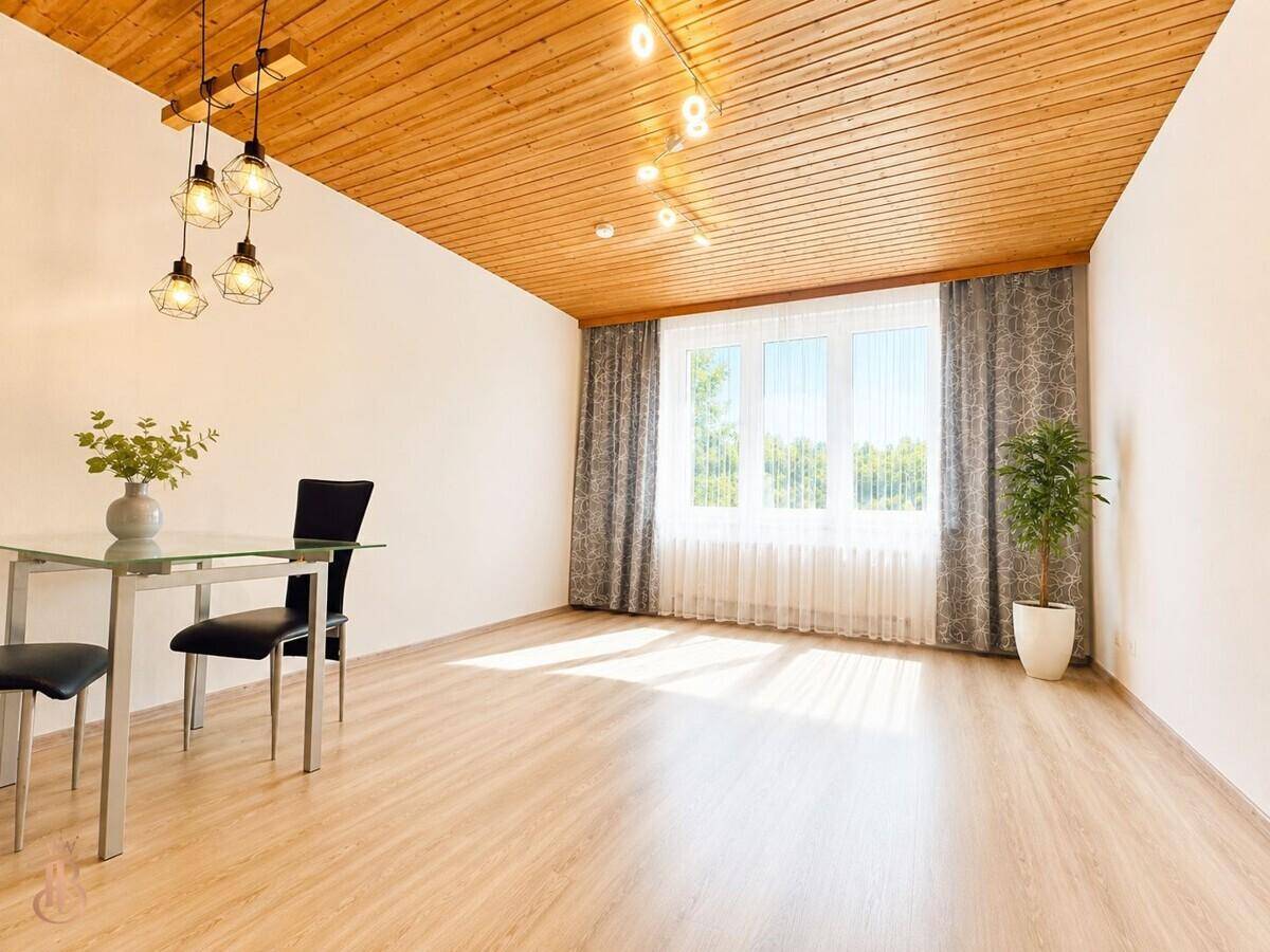 Heller Wohnbereich mit Holzbalkendecke, Laminatboden und großem Fenster mit Blick ins Grüne.