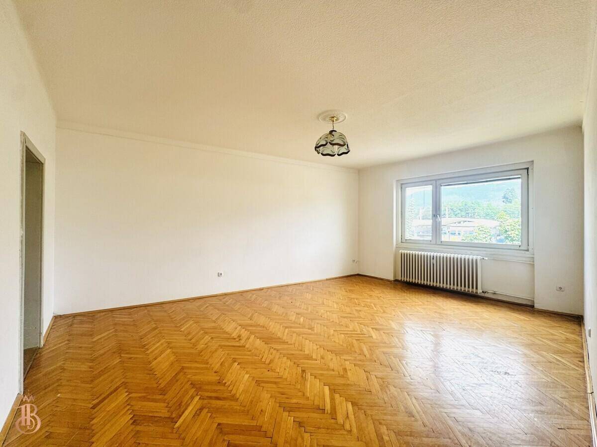 Helles Zimmer mit klassischem Fischgrätparkett, weißer Decke und Fenster mit Ausblick.
