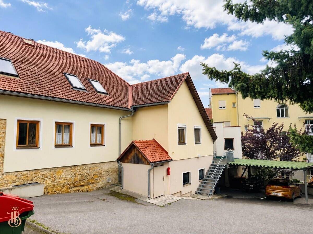Rückansicht des Gebäudes mit Außentreppe und überdachtem Carport.