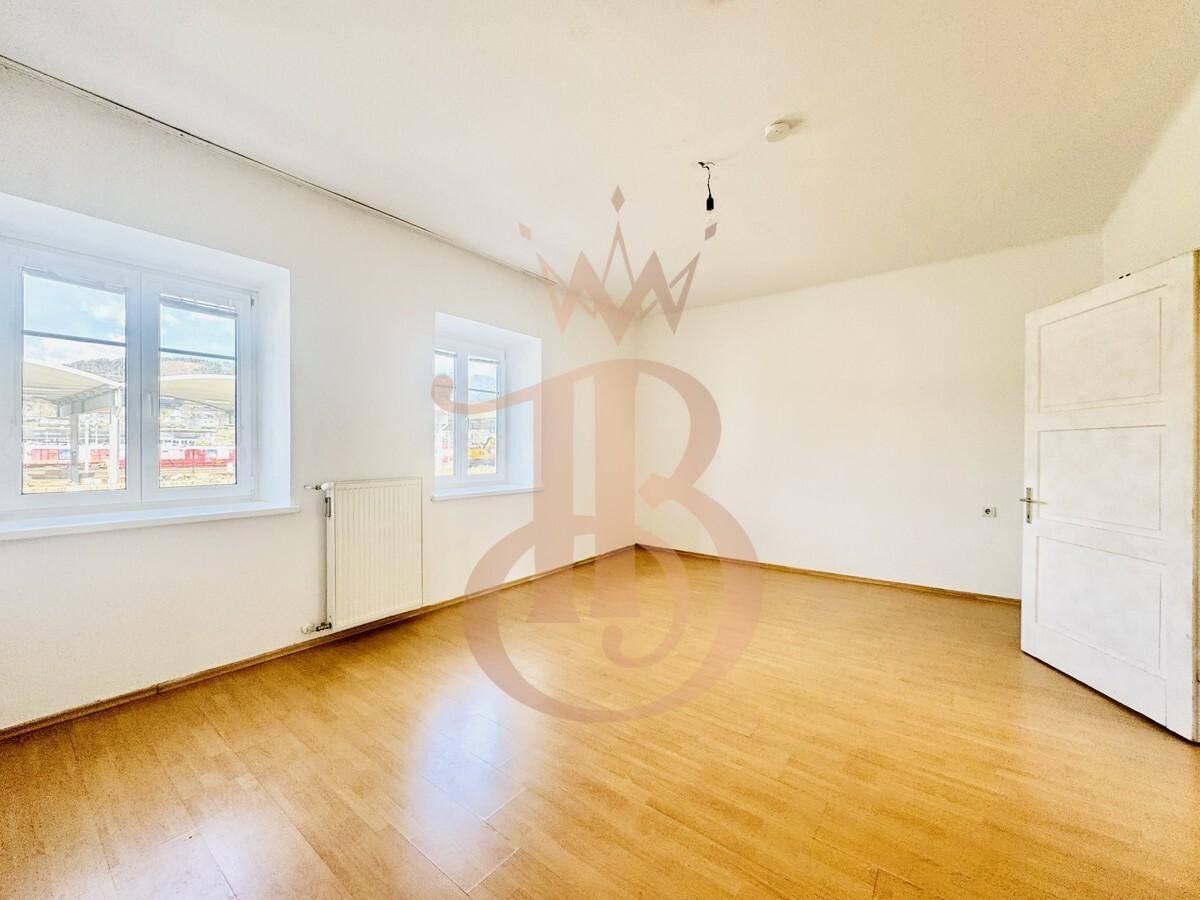 Leeres Zimmer mit hellem Laminatboden und zwei Fenstern, ideal als Wohn- oder Schlafzimmer.