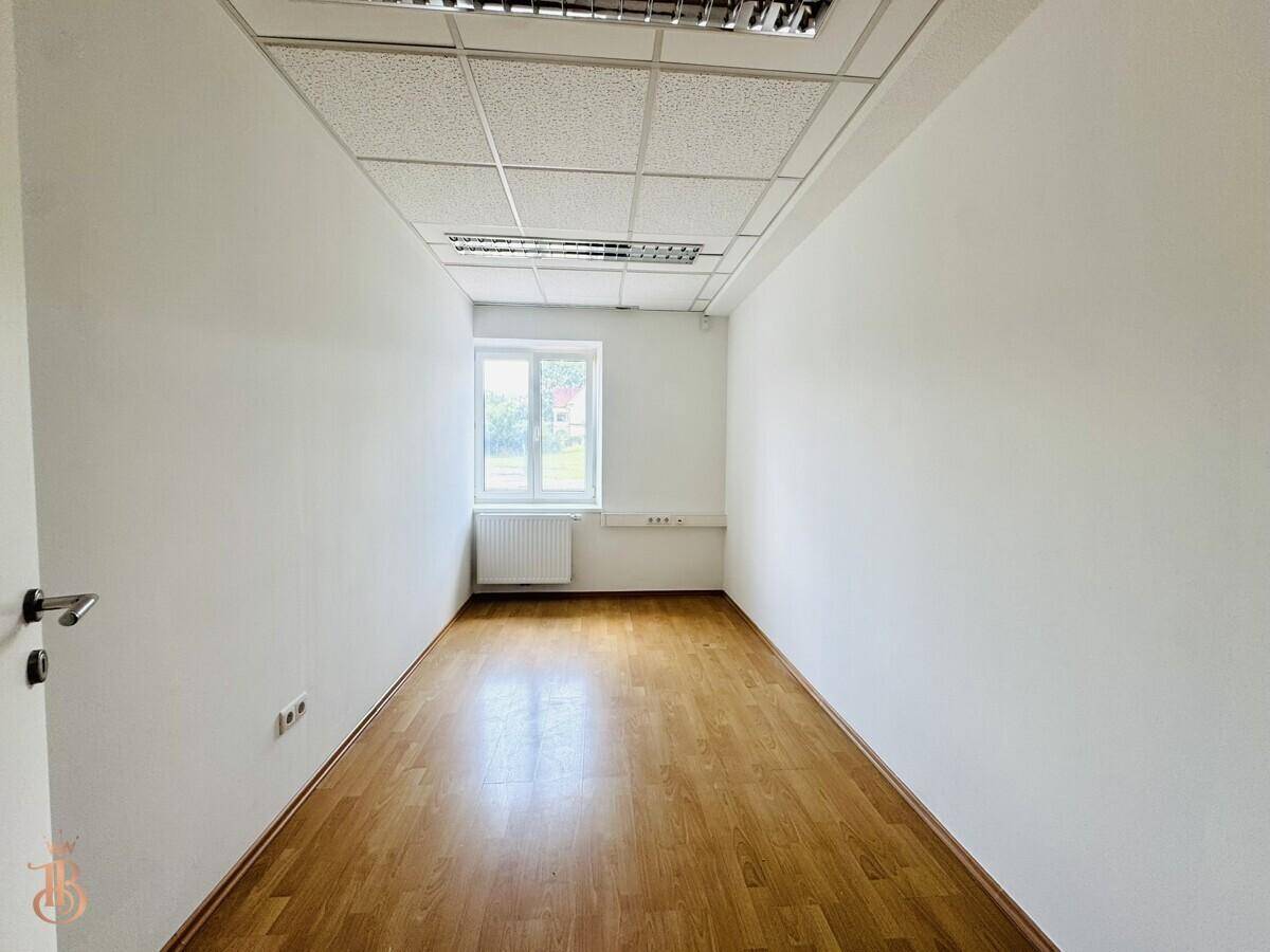 Heller Büroraum mit Holzfußboden, weiß gestrichenen Wänden und einem Fenster.