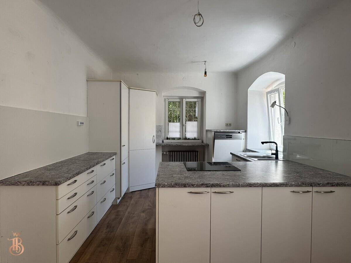 Funktionale Küche mit weißen Unterschränken, integriertem Kochfeld und Fenster mit Tageslicht.