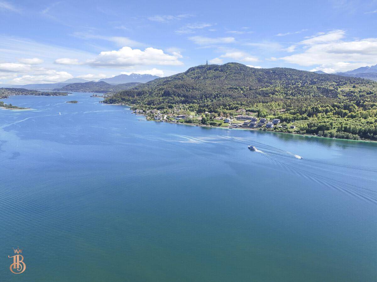 Luftaufnahme des Sees mit einem Boot auf dem Wasser und der malerischen Bergkulisse im Hintergrund.