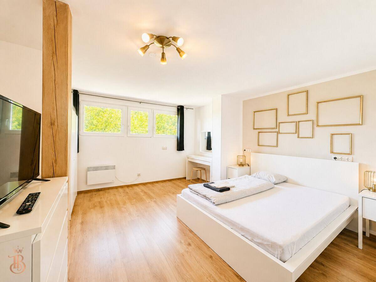 Helles Schlafzimmer mit Doppelbett, Schreibtisch und großen Fenstern für eine angenehme Atmosphäre.