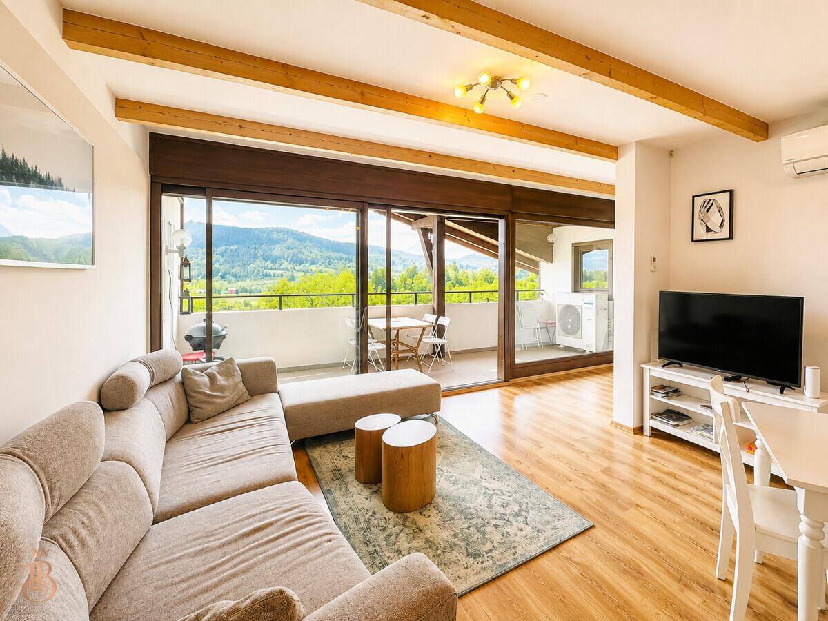 Gemütliches Wohnzimmer mit Sofa, Fernseher und Blick auf die Berge vom angrenzenden Balkon.