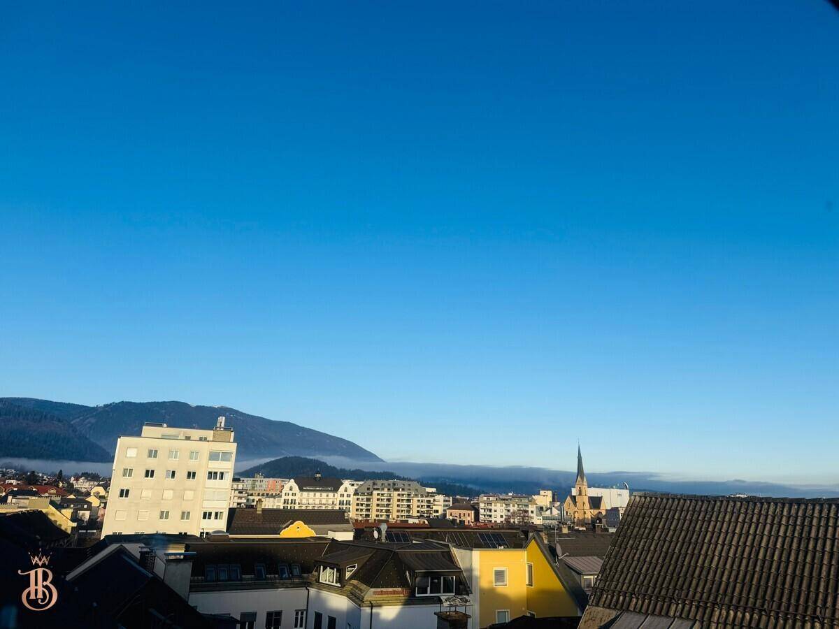 Klarer Blick über die Stadtlandschaft mit Gebäuden und einer Bergkette im Hintergrund.