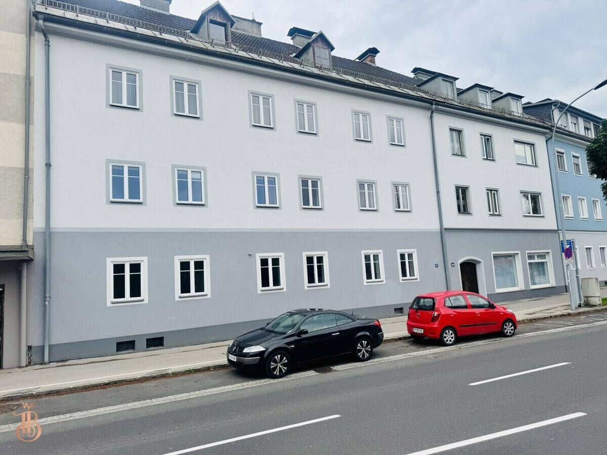 Straßenansicht eines Mehrfamilienhauses mit geparkten Fahrzeugen und einer klaren Fassade.
