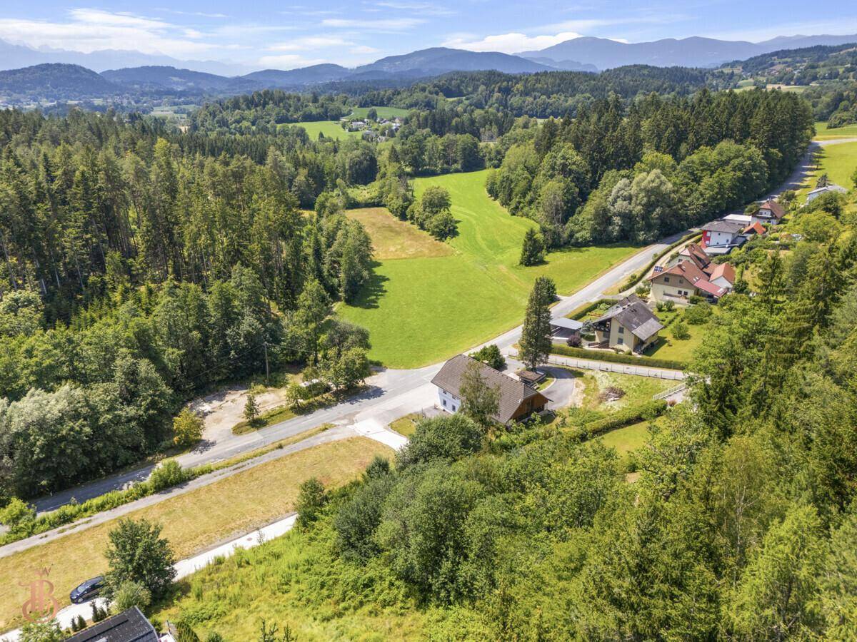 Panoramablick auf eine ländliche Siedlung mit Feldern, Wäldern und Bergen im Hintergrund.