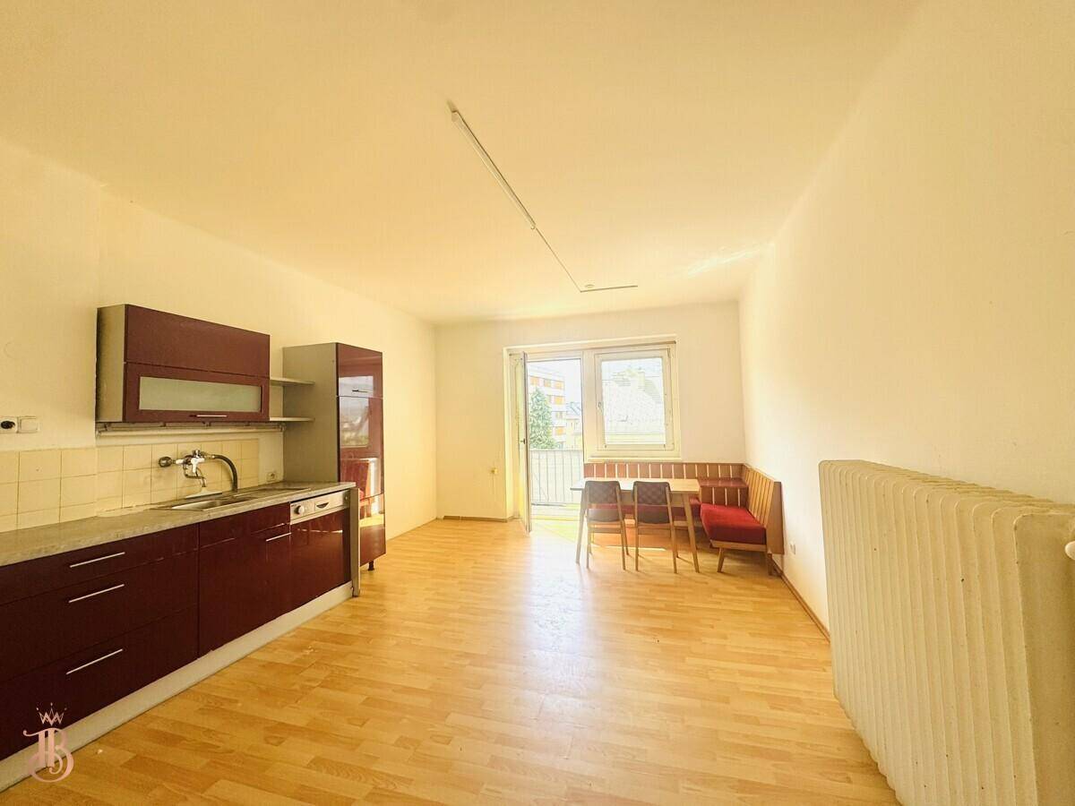 Heller offener Wohn-Essbereich mit integrierter Küchenzeile und Zugang zum Balkon.