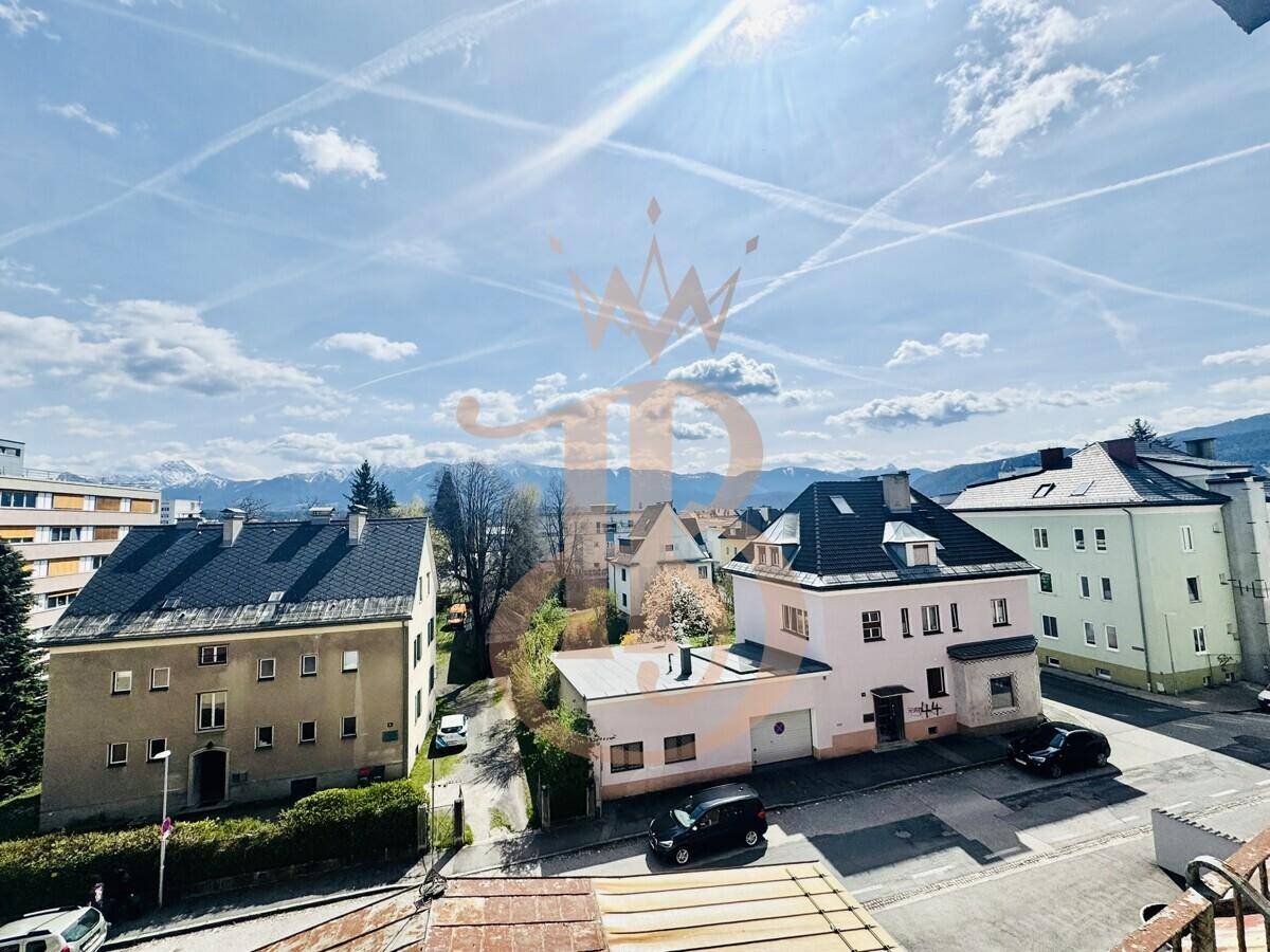 Sonniger Ausblick auf eine Wohnstraße mit verschiedenen Gebäuden und den majestätischen Bergen in der Ferne.