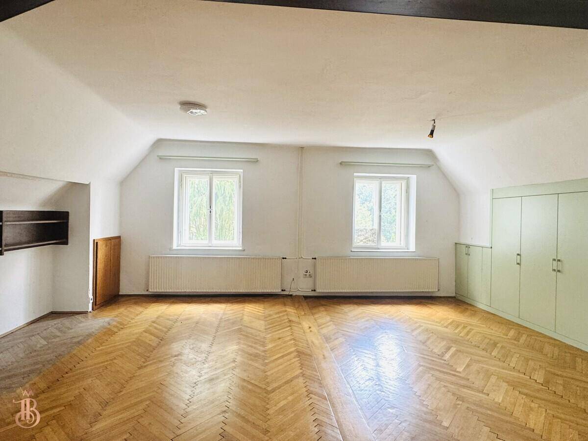 Geräumiges Dachzimmer mit Fischgrätparkett, Dachschrägen und Einbauschränken.
