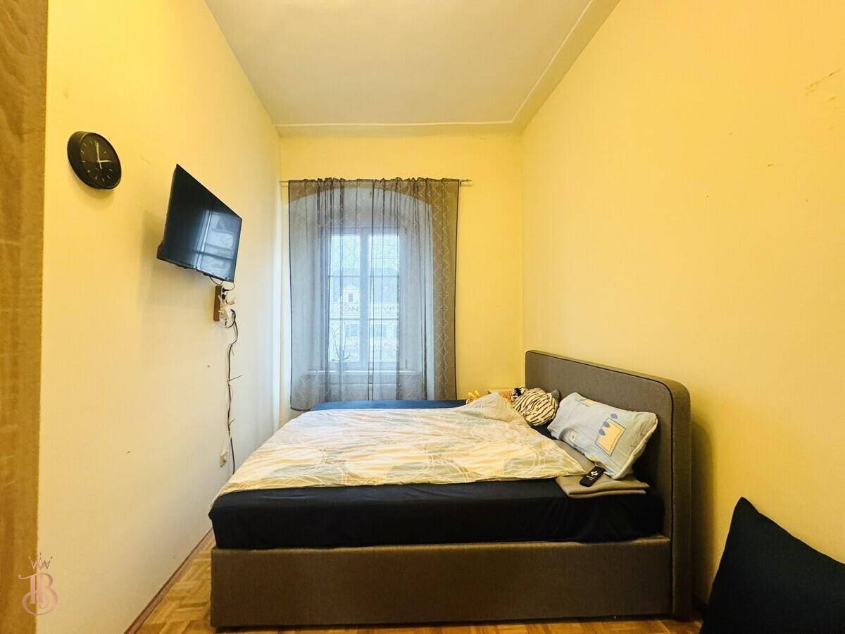 Kleines Schlafzimmer mit Bett, Wandfernseher und Holzboden, funktional und gemütlich.