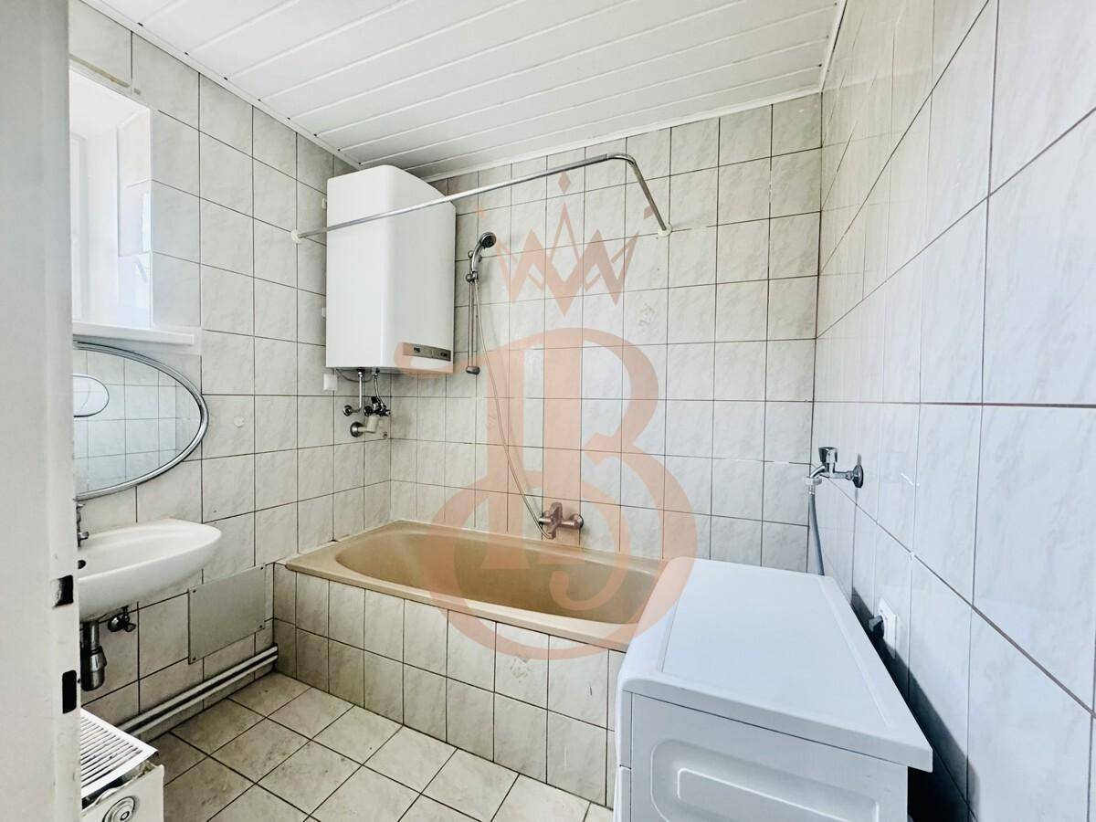 Badezimmer mit Badewanne, Waschbecken und Waschmaschine, umgeben von weißen Fliesen.