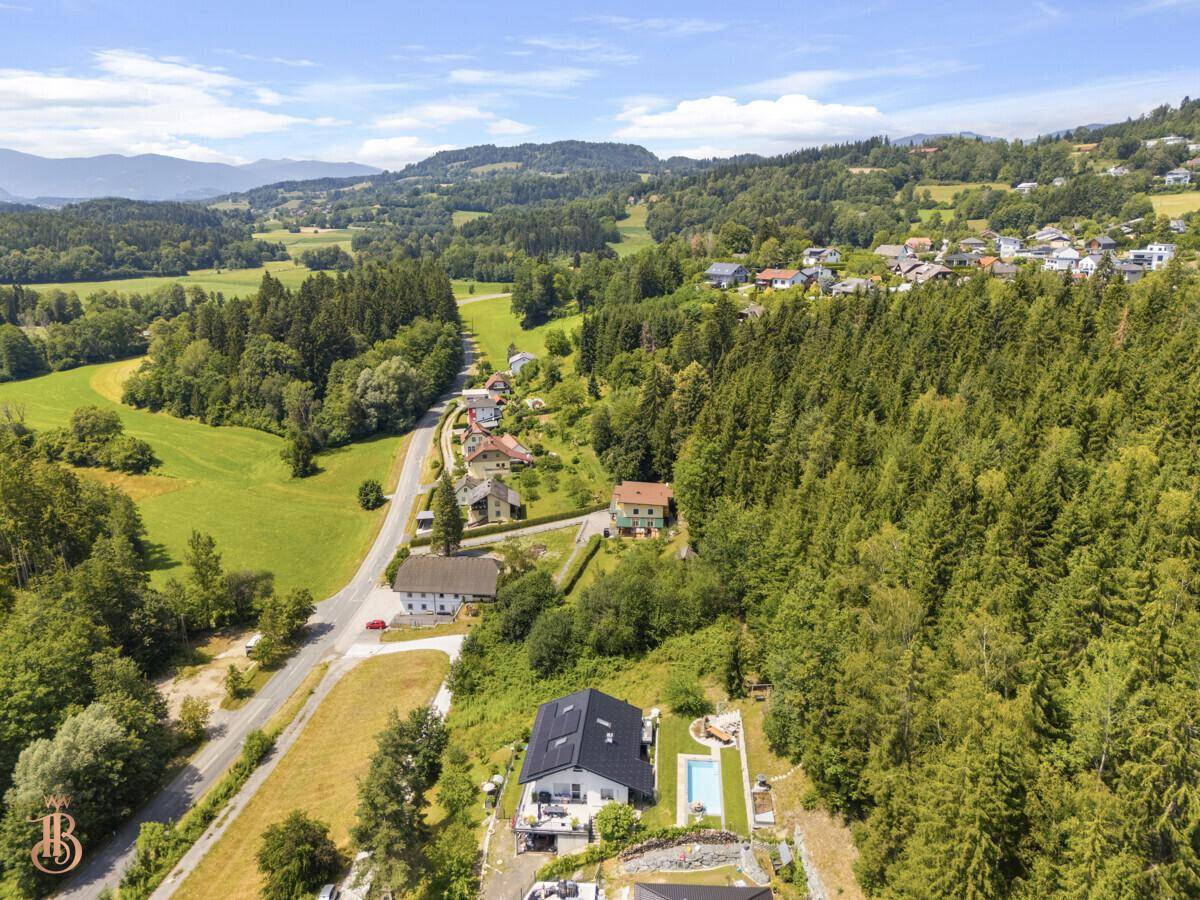 Luftaufnahme einer Wohnsiedlung mit Häusern, Gärten, einem Pool und weitem Blick auf die Berge.