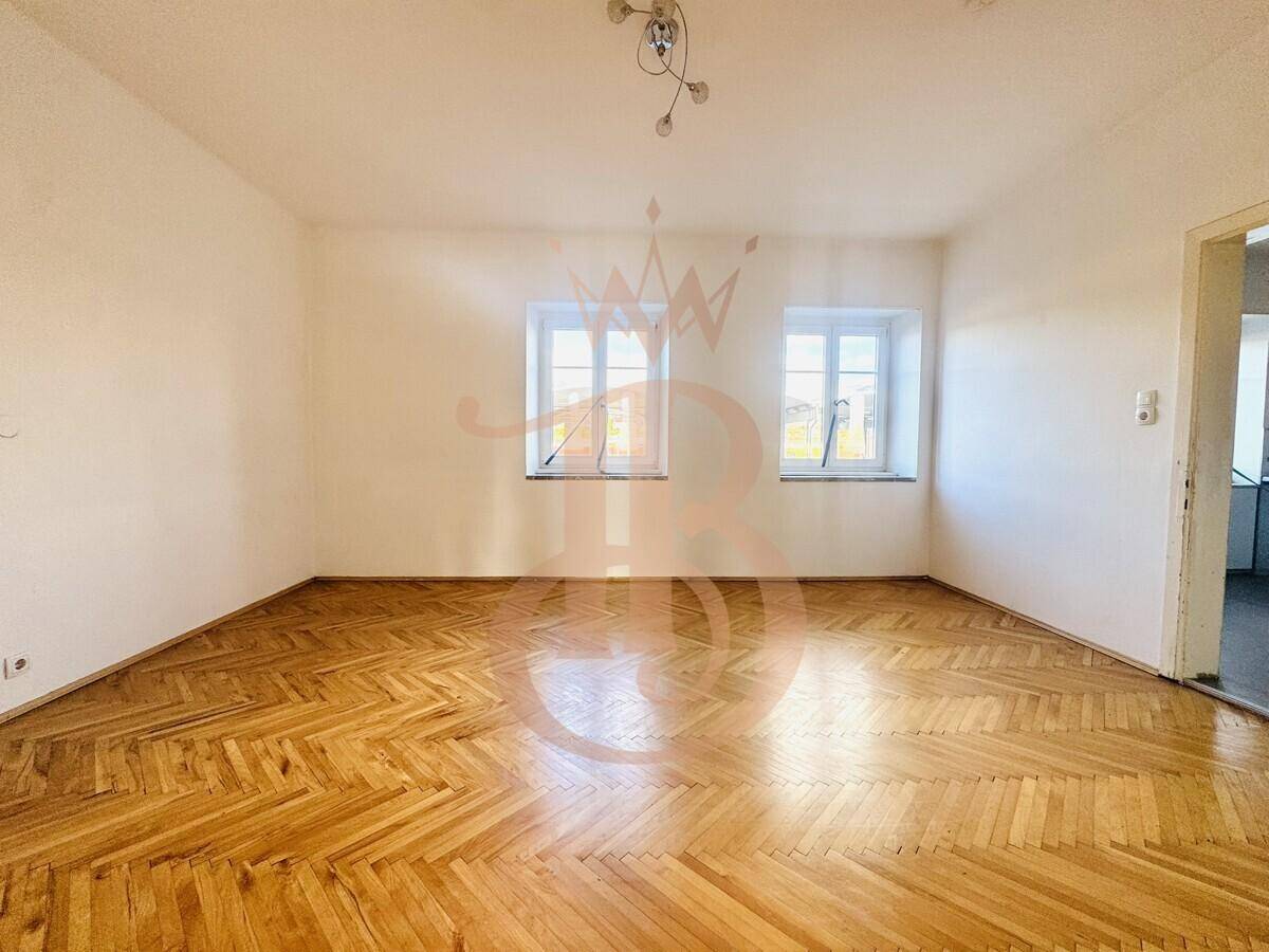 Helles Zimmer mit Fischgrätparkettboden und zwei Fenstern, das viel Tageslicht erhält.