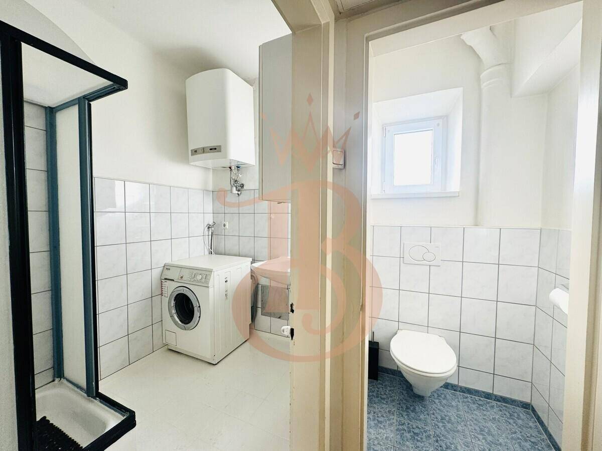 Badezimmer mit Duschkabine, wandhängender Toilette und Waschmaschine, hell gefliest und funktional.