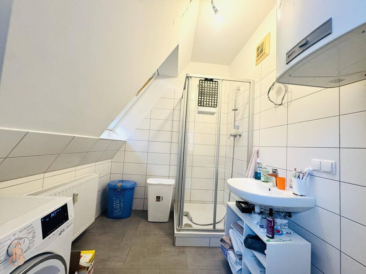 Badezimmer mit Dusche, Waschbecken, Waschmaschine und Dachfenster, funktional und hell.