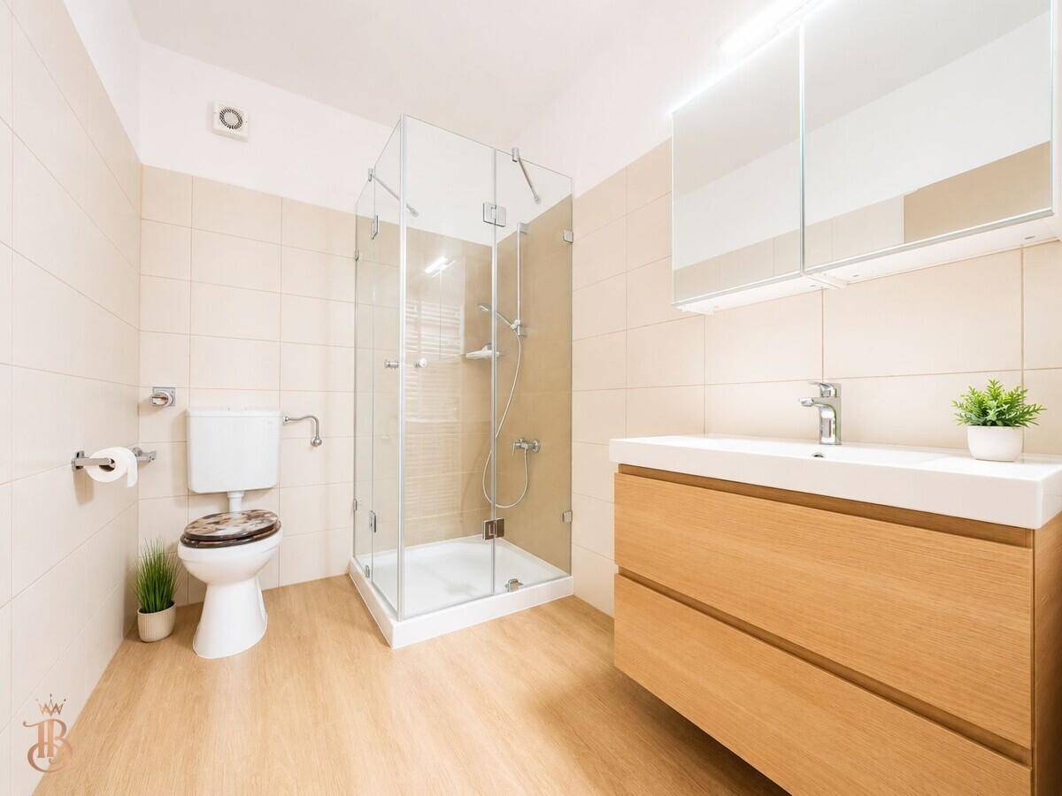 Modernes Badezimmer mit beigefarbenen Fliesen, Glasduschkabine und Holzwaschtisch mit Unterschrank.