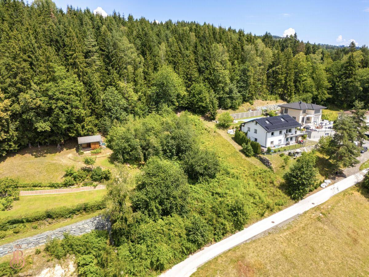 Grundstück in Hanglage, umgeben von üppigem Grün und benachbarten Wohnhäusern.