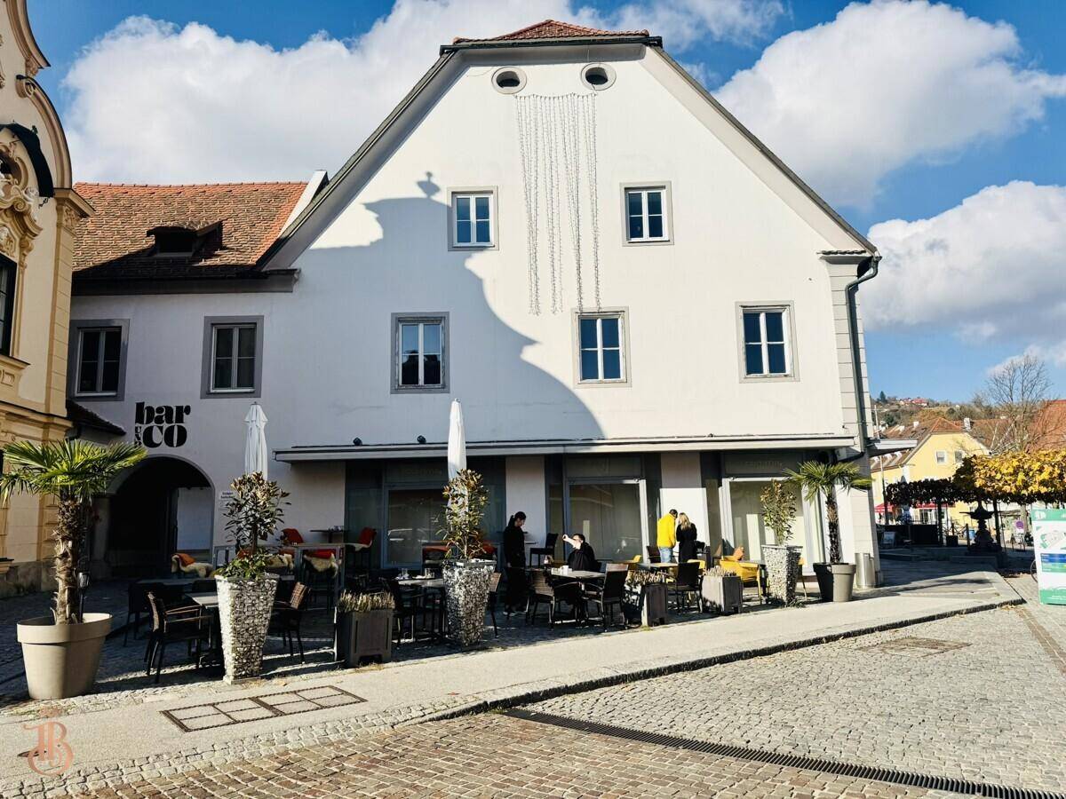 Weißes Gebäude mit Bar und Außenterrasse an einem sonnigen Tag in der Stadt.