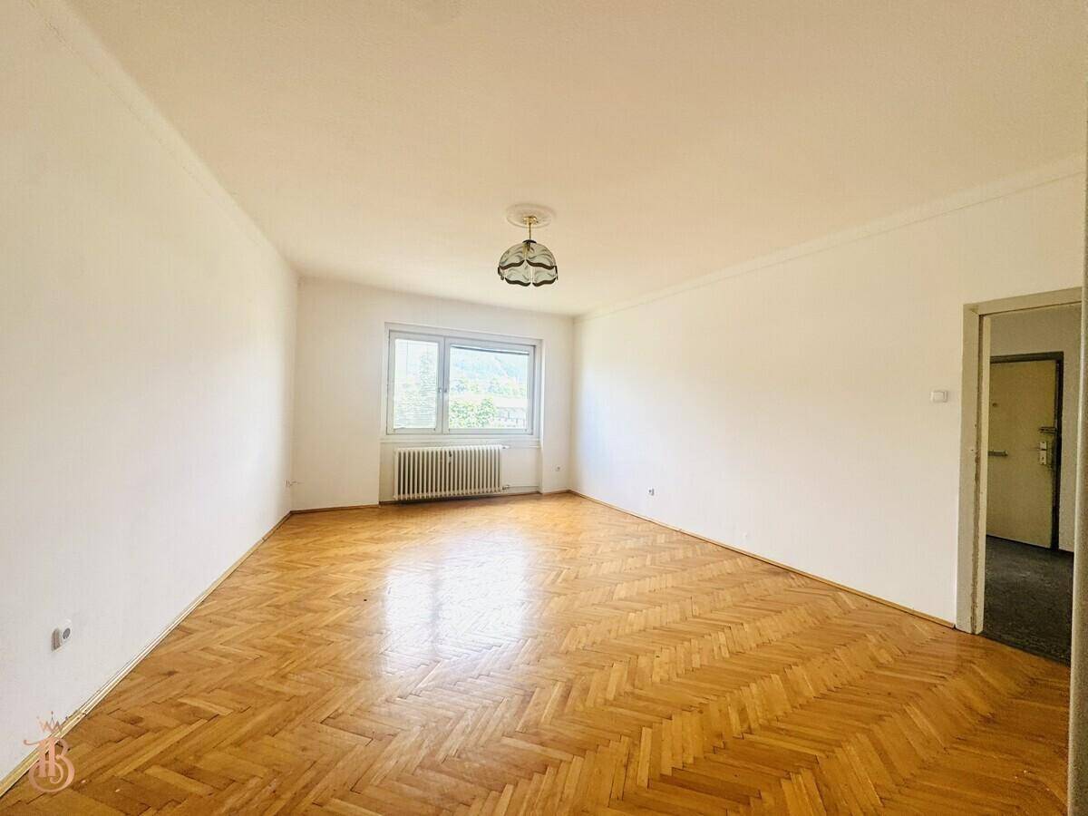 Großes, helles Zimmer mit Fischgrätparkett und einem Fenster, das viel Tageslicht hereinlässt.