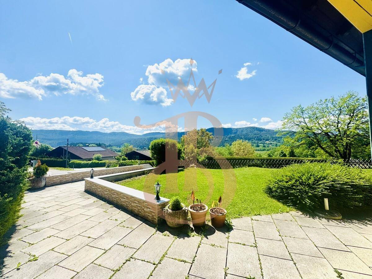 Gepflasterter Außenbereich mit Rasenfläche und Blick auf die umliegende Berglandschaft.