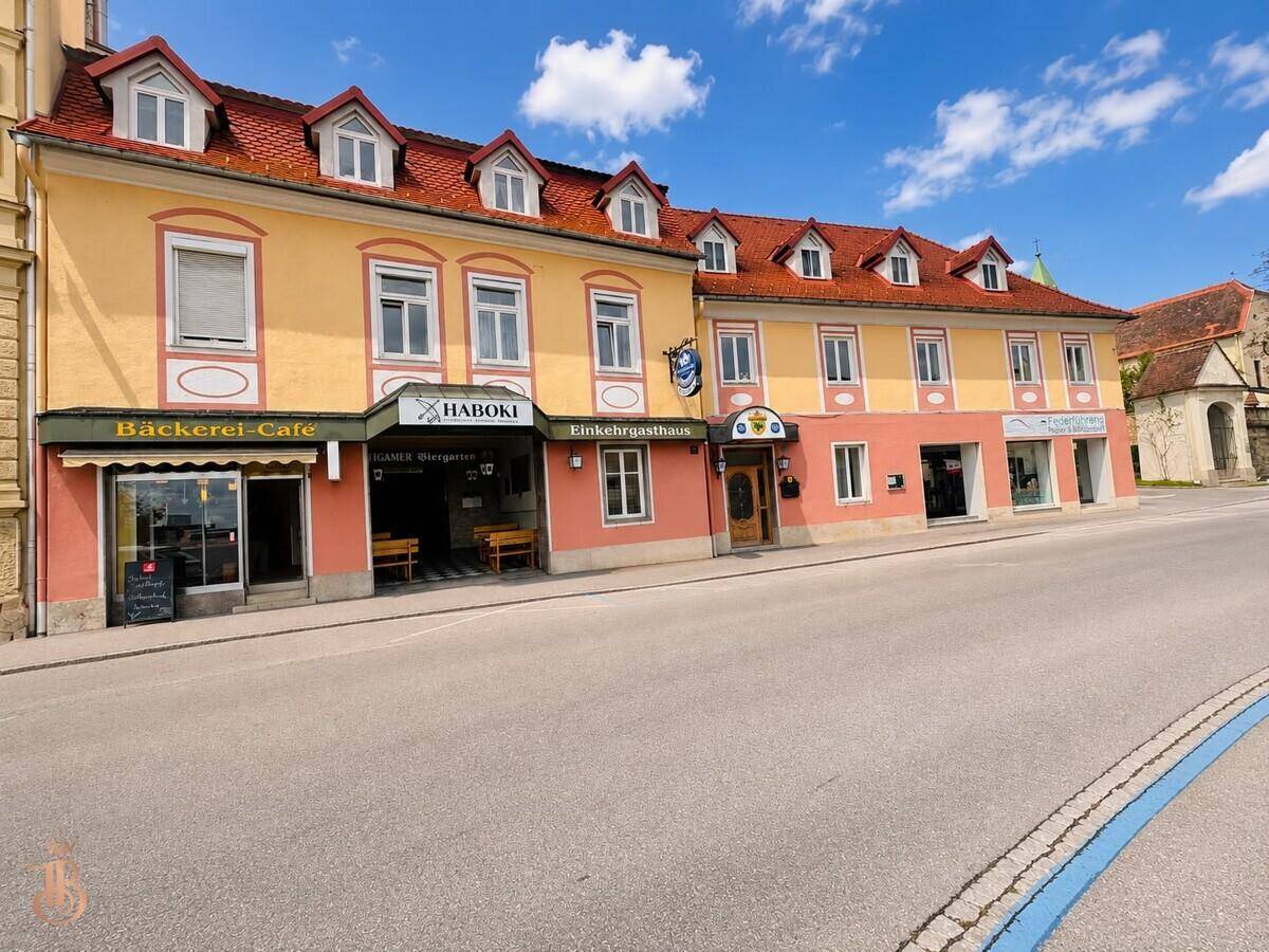 Gebäudeansicht mit Bäckerei-Café und Gasthaus im Erdgeschoss unter blauem Himmel.