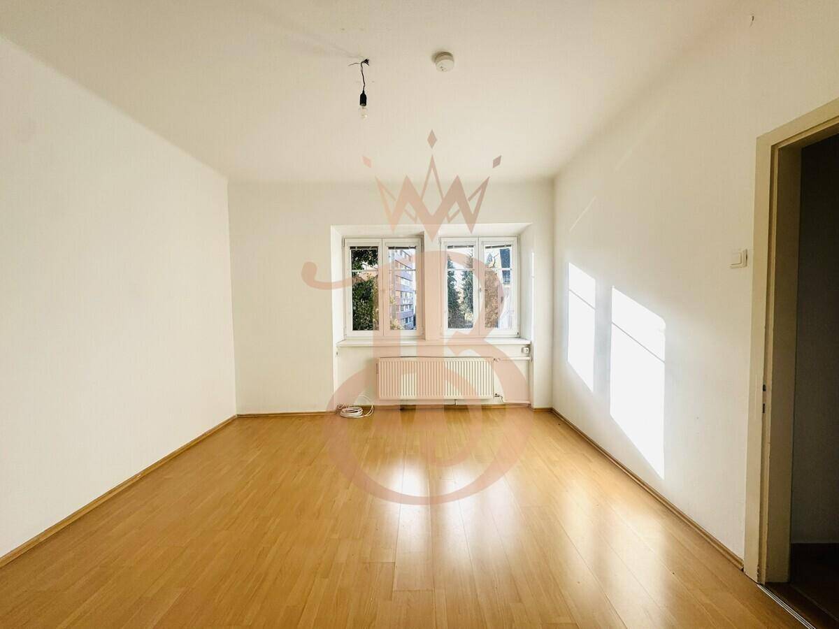 Helles Zimmer mit hellem Laminatboden und zwei Fenstern, das viel Tageslicht hereinlässt.