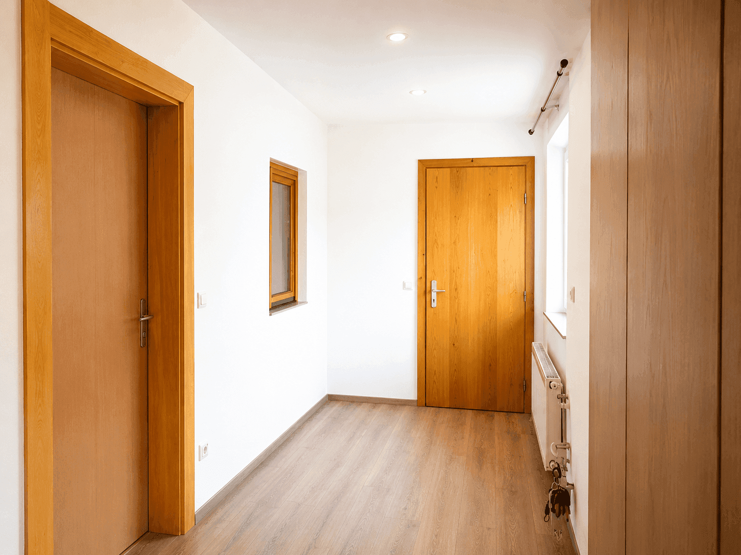Heller Flur mit Holztüren, hellem Laminatboden und einem kleinen Fenster.