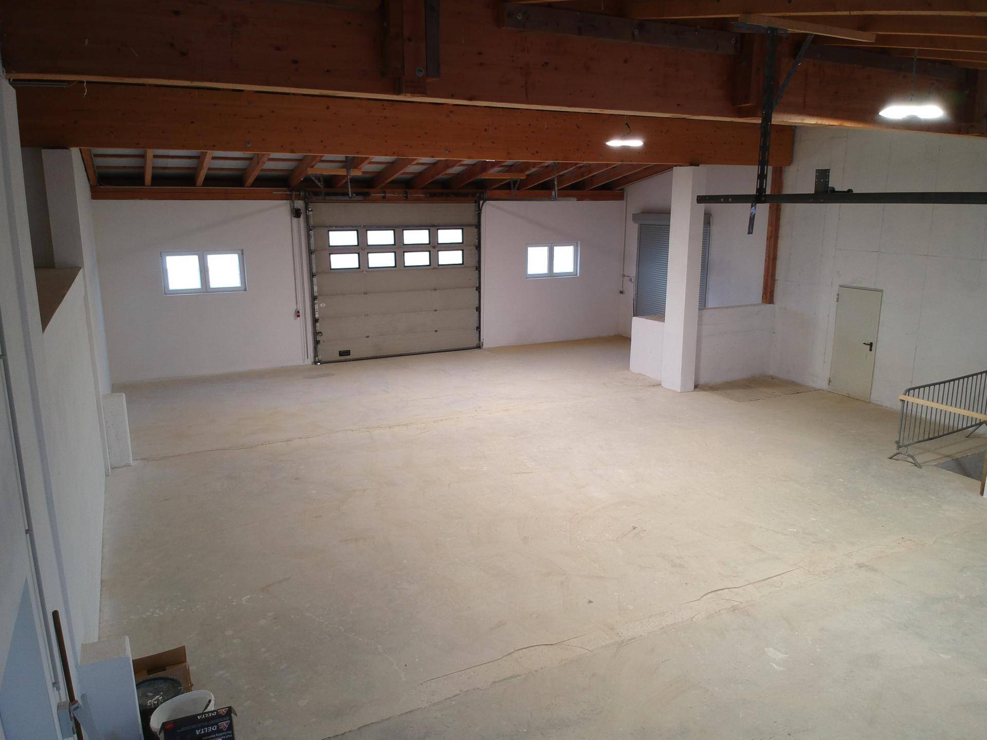 Geräumige Lagerhalle mit hohen Decken, Holzbalkenkonstruktion und einem großen Garagentor.