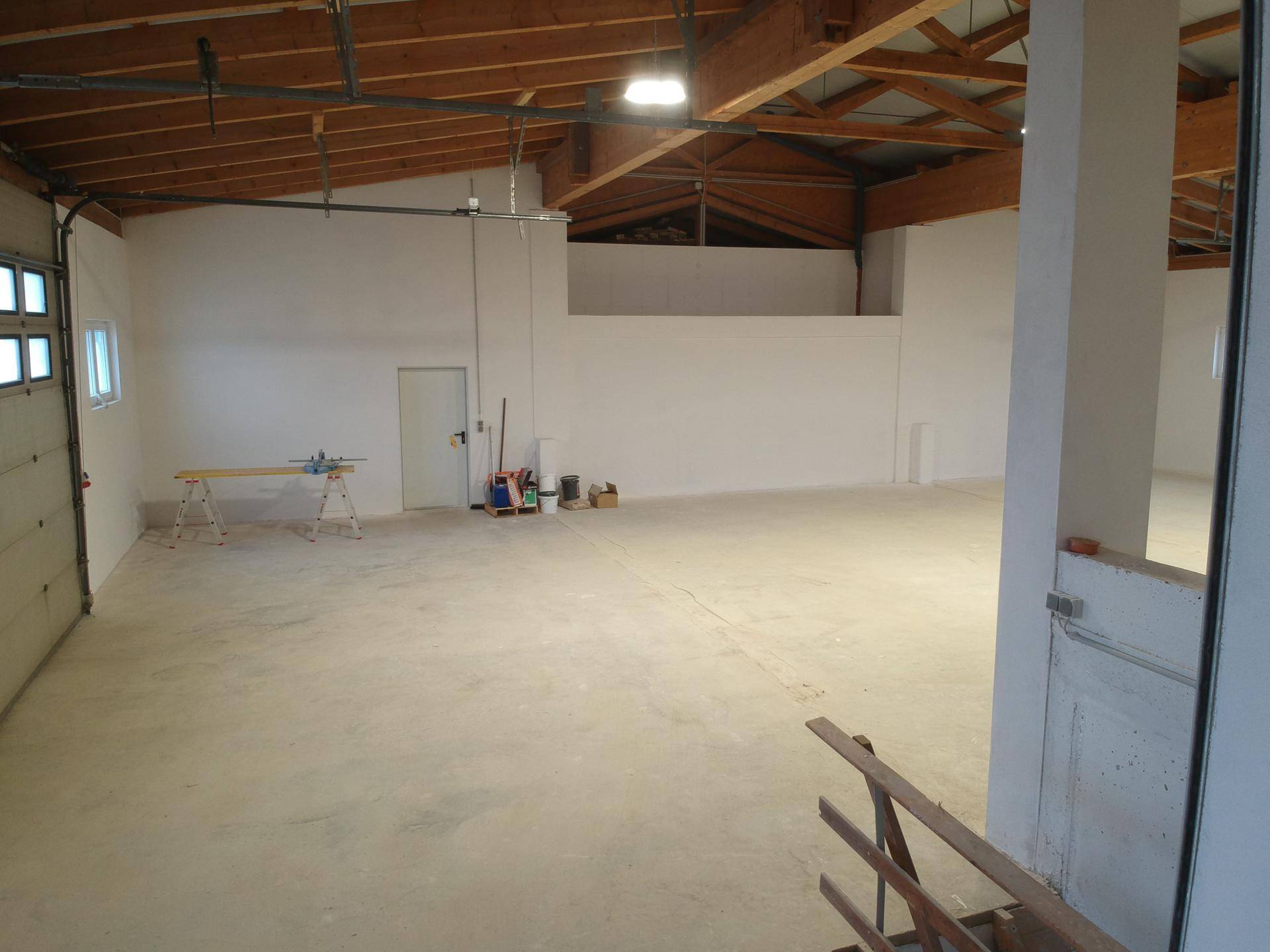 Geräumiger Lagerbereich mit Betonboden, Holzbalken und Sektionaltor, bereit zur Nutzung.