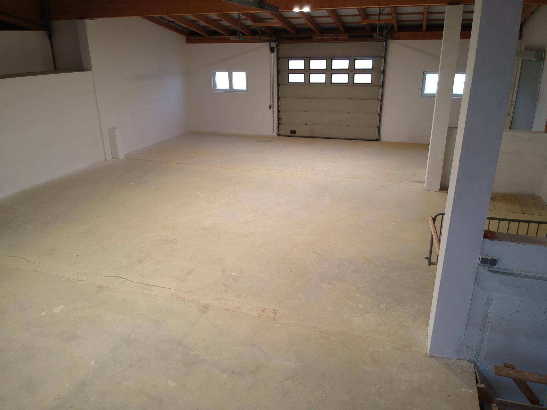 Geräumige Lagerhalle mit Betonboden, hohen Decken und sichtbarer Holzbalkenkonstruktion.