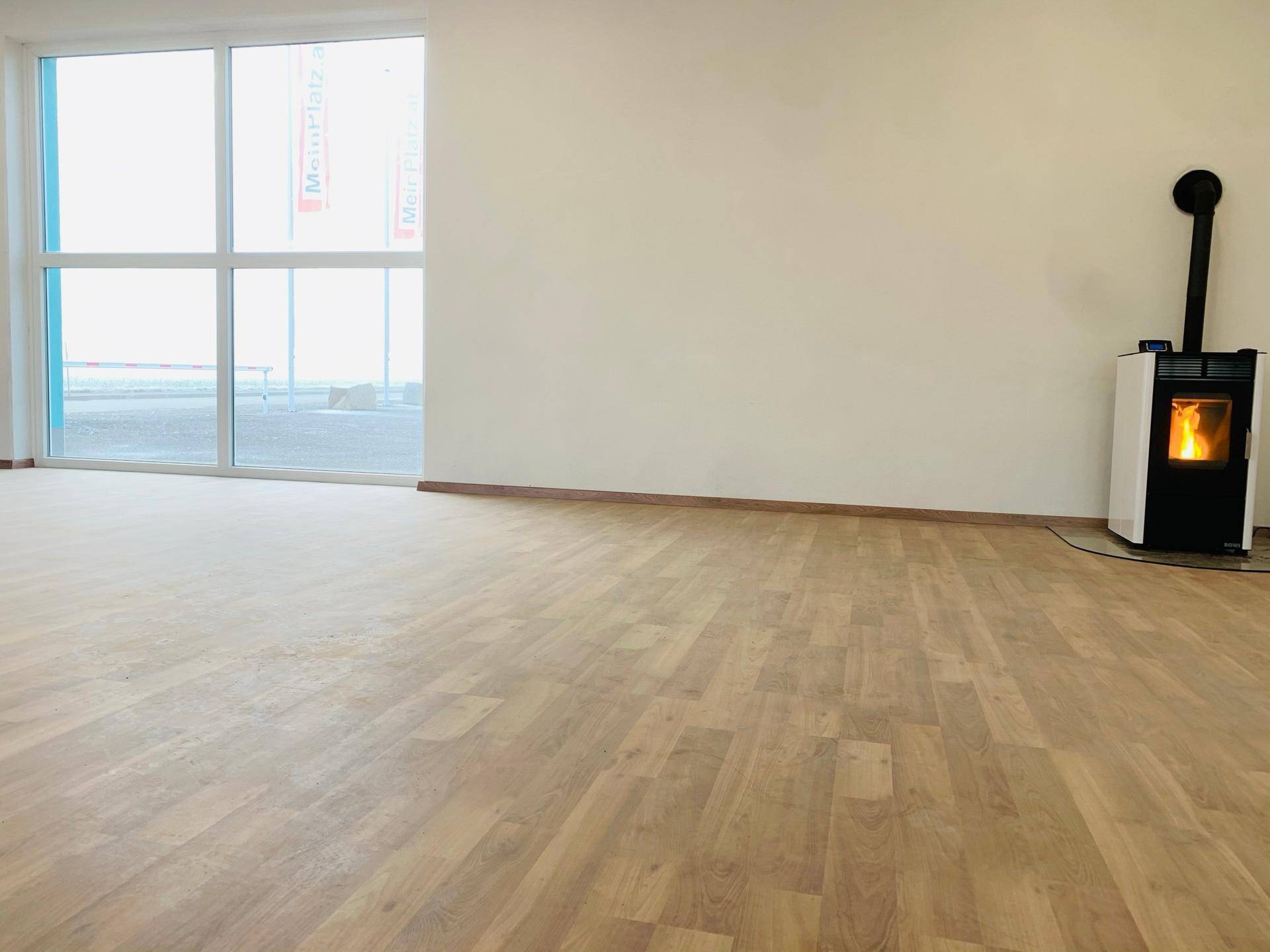 Detailansicht des Laminatbodens und des Pelletofens in einem hellen, modernen Raum mit großem Fenster.