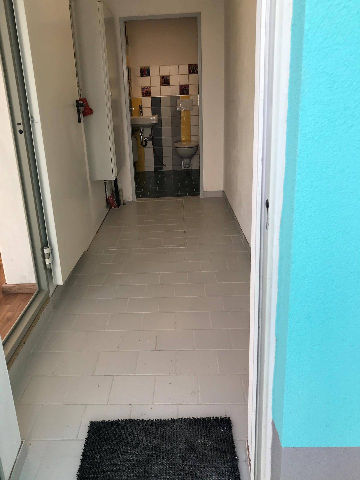 Heller Flur mit Fliesenboden, der zu einem bunten Gäste-WC führt.